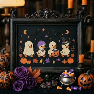 May include: A framed cross-stitch embroidery on black fabric featuring four ducklings in Halloween costumes, including a ghost, a purple-haired creature, and a witch, surrounded by orange pumpkins, bats, stars, and moons in a dark ornate frame.