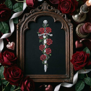 Può includere: Un disegno a punto croce incorniciato con una spada ornata di rose rosse e viti verdi su sfondo nero. La cornice in legno scuro è circondata da rose rosse, candele e nastri.