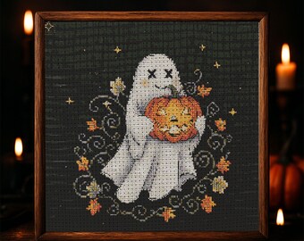 Pode incluir: Obra de arte em ponto cruz de um fantasma amigável segurando uma abóbora esculpida. O fantasma é branco com olhos pretos e a abóbora é laranja. O design é emoldurado em uma moldura de madeira escura, com um fundo escuro e folhagem com tema de outono.