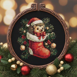 May include: A cross-stitch design of a hedgehog wearing a Santa hat and bow tie, inside a red Christmas stocking. The design is framed in a wooden embroidery hoop, surrounded by Christmas ornaments and greenery.