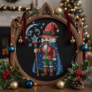 Può includere: Un ricamo a punto croce incorniciato di uno schiaccianoci mago con un cappotto rosso e un mantello blu, che tiene in mano un bastone a forma di stella. La cornice è in legno scuro con un design ad arco gotico, decorata con ornamenti e agrifoglio. Un albero di Natale sullo sfondo.