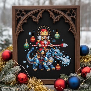 May include: Cross-stitch art of a nutcracker riding a blue dragon, framed in a dark wood gothic-style frame. The nutcracker wears a red uniform and gold crown. The dragon breathes a frosty cloud. Christmas ornaments surround the frame.