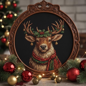 May include: A cross-stitch artwork of a reindeer wearing a festive scarf and a holly wreath, framed in a dark brown, ornate oval frame. The reindeer has golden bells hanging from its antlers. Christmas ornaments and greenery surround the frame.
