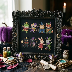 May include: A cross-stitch embroidery on black fabric featuring eight colourful animal characters in costumes, framed in an ornate black gothic-style frame with bat and moon motifs. The characters include a frog, mouse, owl, fox, cat, crow, rabbit, and goat.