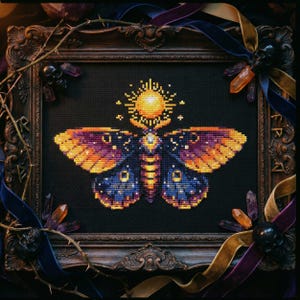 May include: Cross-stitch artwork of a moth with orange, purple, and blue wings, framed in a dark wooden ornate frame. The moth has a sun-like design above its head. The frame is decorated with crystals, ribbons, and small skulls.
