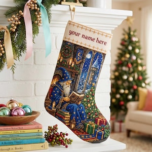Op de afbeelding: Een kerstkous met een kruissteekafbeelding van een tovenaar in een blauwe mantel die een boek leest bij een open haard en een versierde boom. De bovenrand is crèmekleurig met de tekst your name here geborduurd in donkerrode letters.