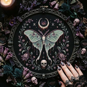 May include: A cross-stitch embroidery featuring a Luna moth with green and purple wings, surrounded by floral elements and a crescent moon. The design is set in a dark, ornate frame, with small skulls and purple flowers around the border.