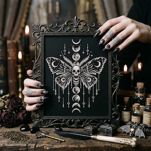 May include: Black framed artwork featuring a detailed white moth design with a skull, crescent moons, and celestial elements. The gothic-style art is held against a dark background, showcasing the intricate cross-stitch pattern. The frame has an ornate, vintage design.