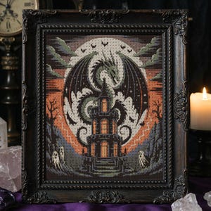 May include: Framed cross-stitch art featuring a dragon, castle, and bats against a night sky. The artwork uses shades of green, orange, and gray, with a dark ornate frame. The image evokes a gothic or fantasy theme.