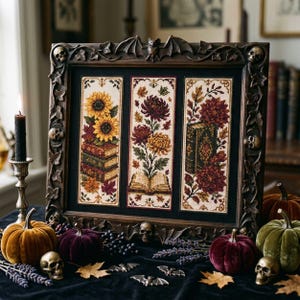 May include: A rectangular dark brown frame with carved skulls, bats, and ivy leaves containing three vertical cross-stitch panels. The panels feature sunflowers, books, chrysanthemums, and an open book on a black background within the frame.
