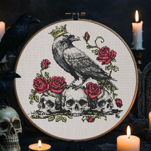 May include: Cross-stitch embroidery featuring a crowned raven perched atop three skulls, surrounded by red roses. The design is set within a wooden embroidery hoop. The color palette includes black, gray, red, and green.
