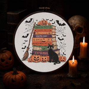 May include: A cross-stitch design in a wooden hoop features a stack of books with Halloween-themed titles, pumpkins, a black cat, bats, and a broom. The books are in shades of orange, purple, and green. A spider web is also included in the design.