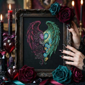 May include: A framed cross-stitch artwork featuring a heart-shaped design composed of two halves, one in deep red and the other in green, resembling angel wings. The artwork is surrounded by dark roses and candles, creating a gothic aesthetic.