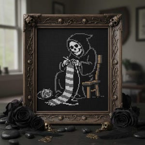 Puede incluir: Arte de punto de cruz en un marco de madera oscura que representa a la Parca tejiendo una bufanda a rayas. El marco está adornado con calaveras. Rosas negras y elementos decorativos rodean la obra enmarcada, creando una estética gótica.