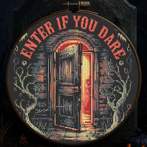 May include: A cross-stitch embroidery in a wooden hoop features a spooky scene. The text "ENTER IF YOU DARE" arches around the top. The image depicts an open door with a bright light, surrounded by a brick wall and gnarled trees.