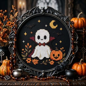 May include: A cross-stitch embroidery featuring a white ghost wearing a red bowtie and cape, centered on black fabric. The design includes a yellow crescent moon, stars, bats, and an orange jack-o'-lantern, all encased in a dark ornate frame.