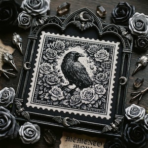 May include: Black and white cross-stitch art featuring a raven surrounded by roses. The artwork is framed in a gothic-style frame with bat and crescent moon accents. The words "Memento Mori" are visible at the bottom.