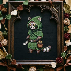 May include: Cross-stitch art of a raccoon dressed in a green hooded cloak, holding a knife and a bag of gold coins. The framed artwork has a dark background and is surrounded by decorative elements, including hearts, keys, and roses.