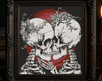 Könnte beinhalten: Kreuzstich-Kunstwerk in einem dunklen, verzierten Rahmen. Das Kunstwerk zeigt zwei weiße Totenköpfe mit floralen Akzenten, vor einem roten Kreis auf schwarzem Hintergrund. Die Totenköpfe sind verschlungen.