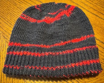 May include: A hand-knitted beanie hat in dark gray with vibrant red stripes. The hat features a ribbed brim and a simple, classic design. This warm winter hat is perfect for cold weather.