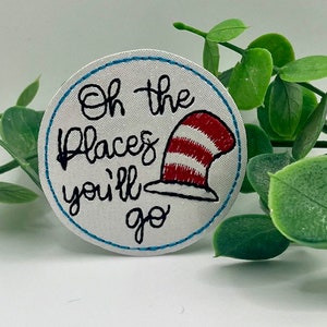 May include: White round embroidered patch with blue stitching around the edge. The patch features the text "Oh the places you'll go" in black cursive font and a red and white striped hat with a red brim.