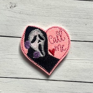 May include: Pink heart-shaped patch with a black and white illustration of a ghost wearing a black hooded robe and a white mask. The ghost is holding a speech bubble that says "Call me".