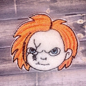 May include: Embroidered patch of a cartoon character with red hair, a white face, and a scar over the left eye. The character has a menacing expression.