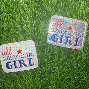 May include: Two silver glitter iron-on patches with the text "all american GIRL" in blue and red embroidery. The patches have a red star in the center.