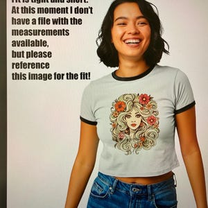 May include: A light gray crop top with black trim and a graphic of a woman with flowers in her hair. The text on the image says, "Please note: this is a new style! Fit is tight and short. At this moment I don't have a file with the measurements available, but please reference this image for the fit!"