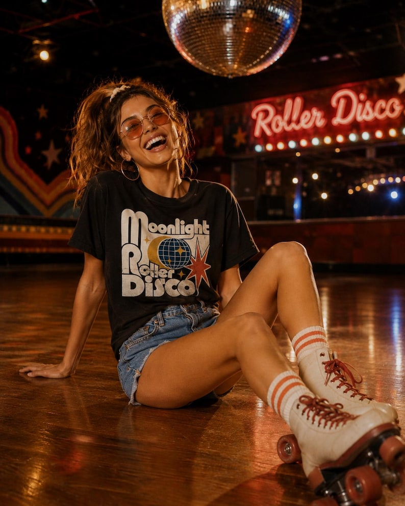 Może przedstawiać: Osoba w czarnym t-shircie z grafiką "Moonlight Roller Disco", dżinsowych szortach i rolkach. Rolki są białe z czerwonymi sznurowadłami i pomarańczowymi k&oacute;łkami. W tle kula dyskotekowa i neonowy znak "Roller Disco".