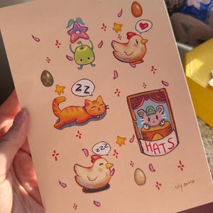 May include: A greeting card with whimsical illustrations of a sleeping orange cat, chickens, a mouse in a hat, and other cute elements. The card has a light pink background with the artist's signature in the bottom right corner.