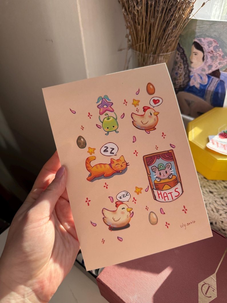 May include: A greeting card with whimsical illustrations of a sleeping orange cat, chickens, a mouse in a hat, and other cute elements. The card has a light pink background with the artist's signature in the bottom right corner.