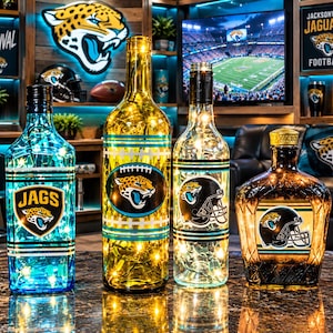May include: Four glass bottles illuminated with internal string lights. The first is blue with a JAGS logo, the second is amber with a football and jaguar logo, the third is clear with a helmet graphic, and the fourth is dark amber with a helmet logo.