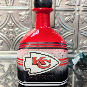 May include: Red, black, and white liquor bottle with a black cap. The bottle has a Kansas City Chiefs logo and the word "PATRON" on it.