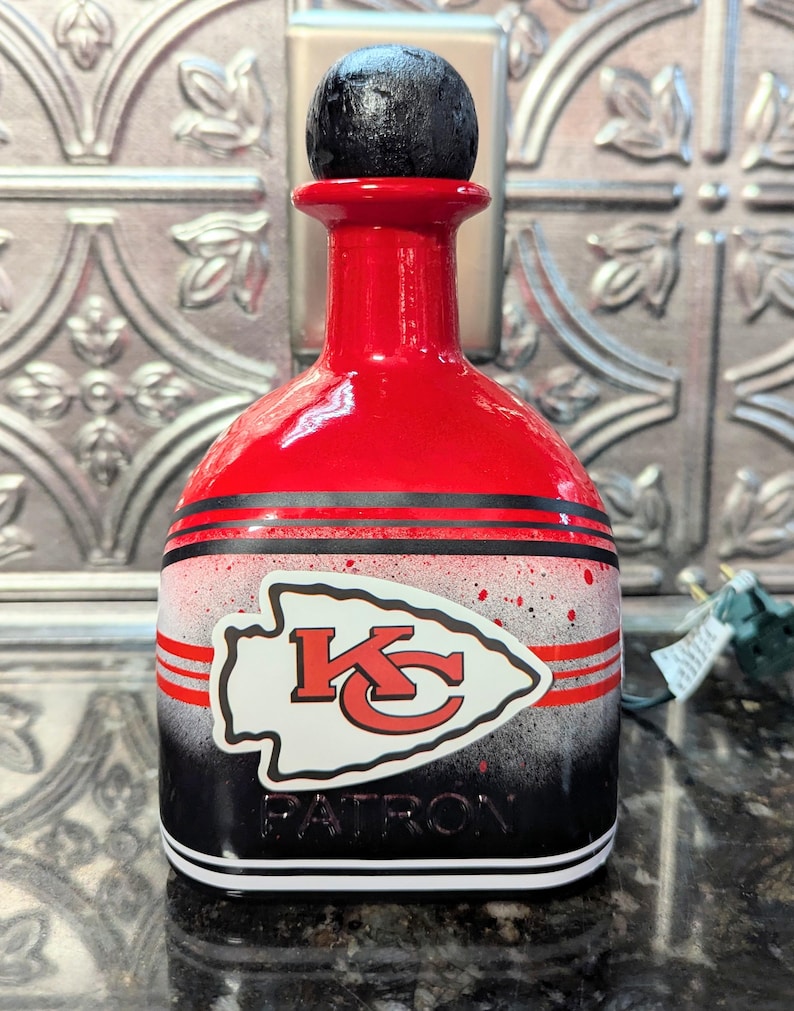 May include: Red, black, and white liquor bottle with a black cap. The bottle has a Kansas City Chiefs logo and the word "PATRON" on it.