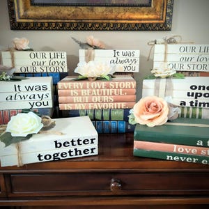 May include: A collection of decorative books with romantic quotes and floral accents. The books are stacked and adorned with phrases like "Our Life, Our Love, Our Story" and "It was always you."
