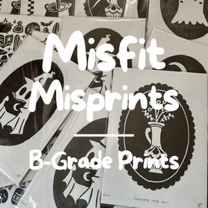 May include: A collection of black and white B-Grade prints, featuring various designs. The prints are packaged in white cardstock. The text "Misfit Misprints" and "B-Grade Prints" are displayed in white, with a variety of illustrations.