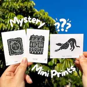 May include: Three small white mini prints with black illustrations are held up against a blue sky and green foliage background. The prints feature a sun, a house, and a dog stretching. The words "Mystery" and "Mini Prints" are written in white.