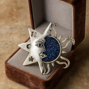 Può includere: Spilla a tema celeste con design a sole e luna argentati e centro blu maculato, presentata in un cofanetto di velluto marrone. La spilla presenta dettagli intricati e un'estetica vintage.