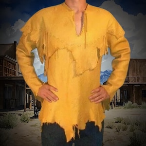 Puede incluir: Camisa de manga larga de color amarillo mostaza con cuello en V y bordes con flecos. La camisa tiene un aspecto rústico y desgastado, con un dobladillo sin rematar y costuras decorativas alrededor del cuello. Las mangas son largas y la camisa parece ser de un material suave.