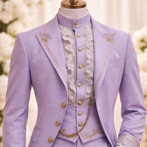 May include: A lavender three-piece suit with gold embroidery and buttons. The suit includes a jacket, vest, and trousers. The white shirt has a high collar and ruffled front. The cuffs of the jacket and the vest are adorned with gold embroidery and lace.