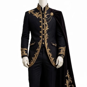 May include: Black formal suit with gold embroidered detailing, including a jacket with ornate trim, matching pants, and a black cape. The jacket features gold buttons and a high collar. The cape is attached with a gold brooch.