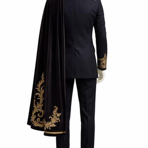 May include: A black suit with gold embroidered accents on the collar, shoulders, and cuffs. A black cape with gold floral embroidery is draped over the suit. The suit is displayed on a mannequin against a white background.