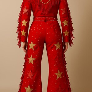 May include: Red jumpsuit with gold star embellishments and fringe detailing. The jacket features a large star design on the back and fringe along the sleeves. The pants are flared and also adorned with gold stars. A belt cinches the waist.