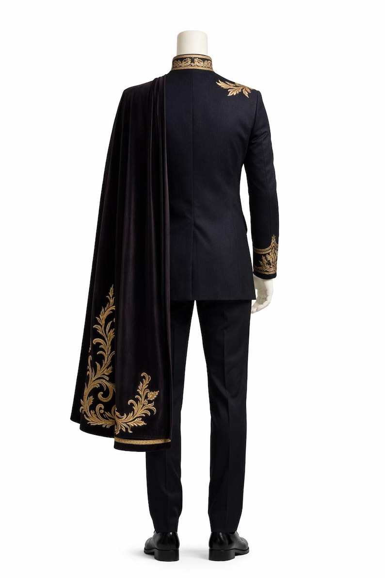 May include: A black suit with gold embroidered accents on the collar, shoulders, and cuffs. A black cape with gold floral embroidery is draped over the suit. The suit is displayed on a mannequin against a white background.
