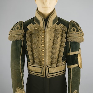 Puede incluir: Una chaqueta de estilo militar en verde oscuro y dorado, con intrincados bordados dorados, borlas y charreteras decorativas. La chaqueta tiene un cuello alto y botones dorados en la parte delantera, mostrando un diseño histórico.