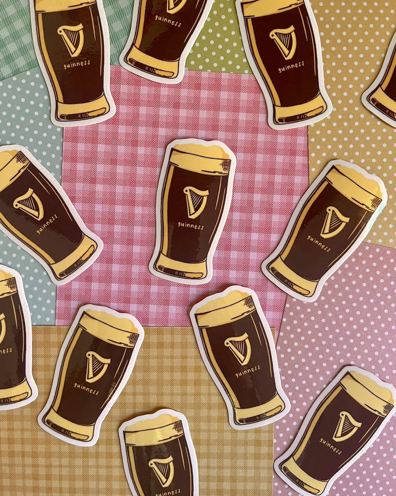 Puede incluir: Una colecci&oacute;n de pegatinas de cerveza Guinness. Cada pegatina presenta una pinta de cerveza oscura con espuma, el logotipo de Guinness y la palabra "Guinness". Las pegatinas est&aacute;n dispersas sobre un fondo de retazos de varios colores y patrones.