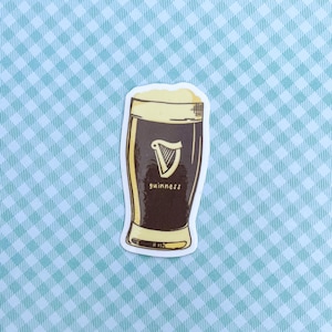 Puede incluir: Una pegatina que representa una pinta de Guinness. El vaso est&aacute; lleno de cerveza oscura y coronado con espuma cremosa. El logotipo de Guinness, un arpa, es visible, con el nombre de la marca debajo.