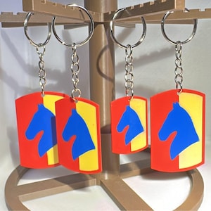 May include: Keychains with a red and yellow background, featuring a blue horse silhouette. The keychains are attached to silver key rings and chains. The horse design is a bold, graphic element.