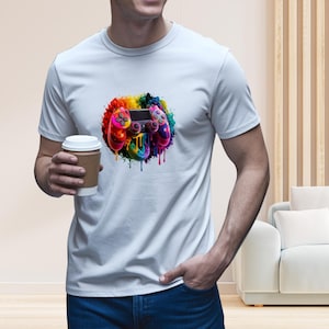 May include: White t-shirt featuring a colorful, abstract design of a video game controller. The controller is rendered in vibrant hues of red, yellow, blue, and purple, with paint-like drips. The shirt is a casual, everyday wear item.